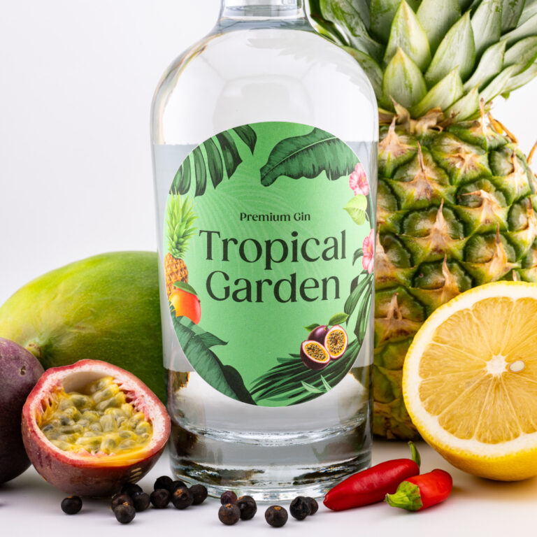 Tropical Garden Gin: Produktfoto mit Flasche zwischen frischen tropischen Früchten wie Maracuja, Ananas und Mango.