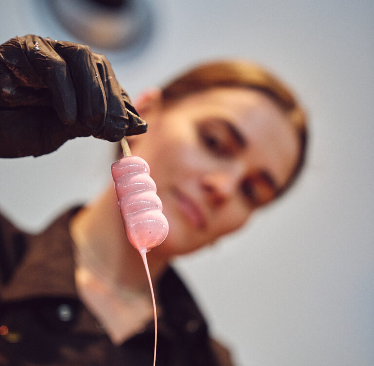 Patissière von Kirberg Catering hält ein frisch glasiertes, rosafarbenes Popsicle in der Hand. Nahaufnahme.