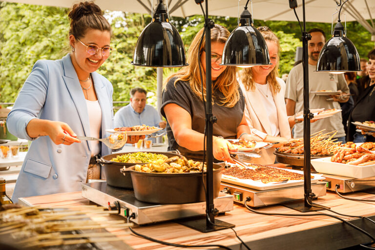 Bei einer Veranstaltung im Freien bedienen sich die Leute lächelnd und genießen die Atmosphäre am Buffet.