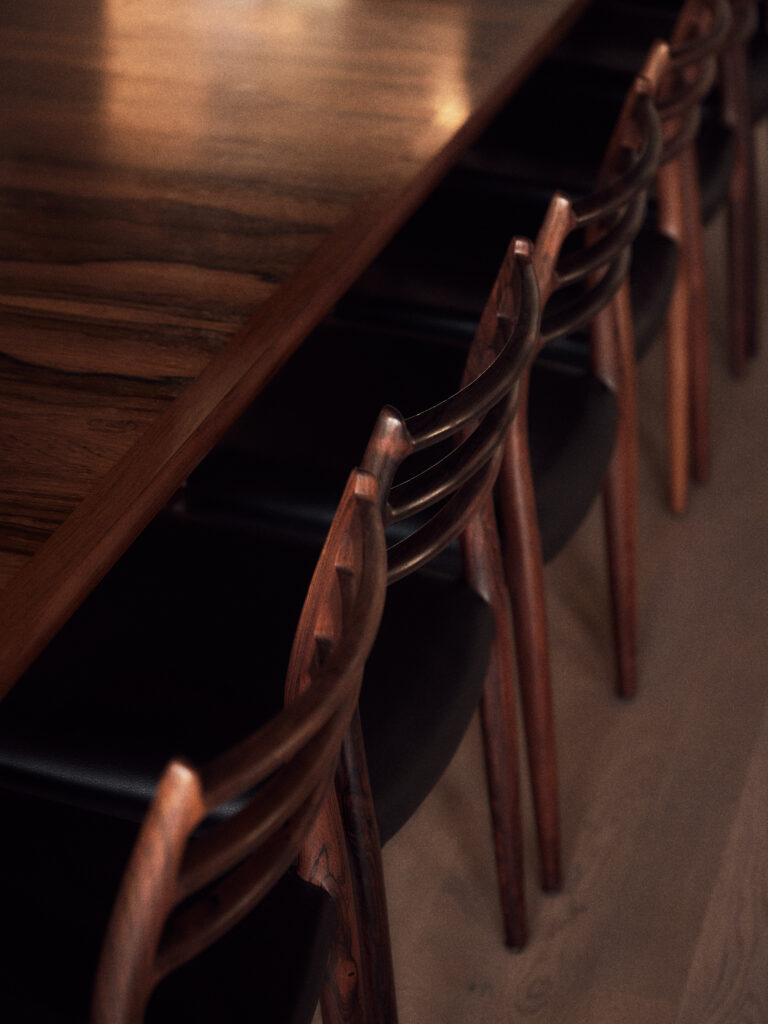 Eine Reihe von Holzstühlen mit dunkler Sitzfläche reiht sich an einen polierten Holztisch im Haus.