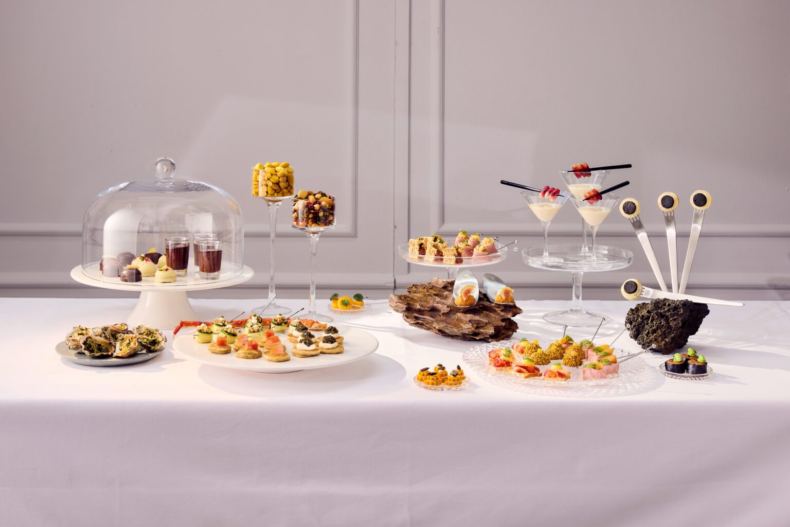 Ein Tisch mit verschiedenen eleganten, mundgerechten Vorspeisen und Desserts auf Ständern aus Glas und Keramik.