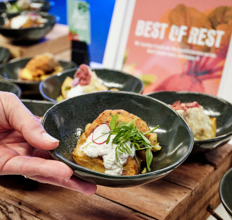 Eine Hand hält eine Schale mit Gourmetgerichten, gekrönt mit Sahne und Grünzeug, auf einem Tisch mit ähnlichen Schalen - mit Regionalen Produkten im Eventcatering für ein authentisches kulinarisches Erlebnis.