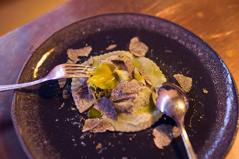 Ein Raviolo mit flüssigem Eigelb, gehobeltem Trüffel, einer Gabel und einem Löffel auf einem dunklen Teller - eines der Highlights im Philara 14 Places.