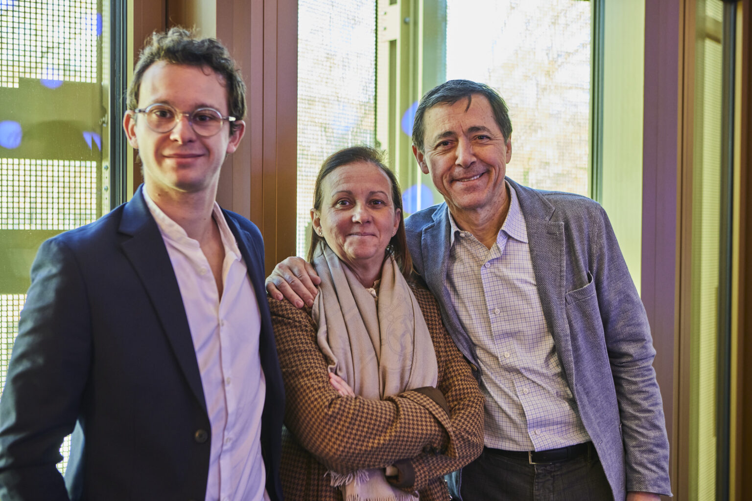 Drei Personen stehen dicht beieinander in einem Innenraum und lächeln in die Kamera in der Nähe großer Fenster des Kirberg Catering Sachsenturm Köln.